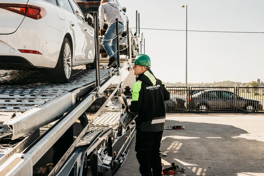 Pracownik w kasku przy platformie autotransportera, widziany z boku i od tyłu.