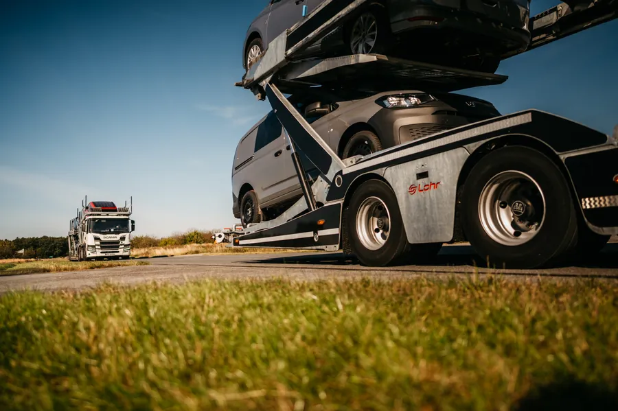Koła i platformy załadowanego autotransportera widziane z boku, z drugim zestawem w tle.