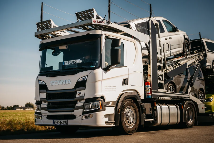 Biała kabina Scania i samochody na załadowanym autotransporterze, sfotografowane z przodu pod kątem.