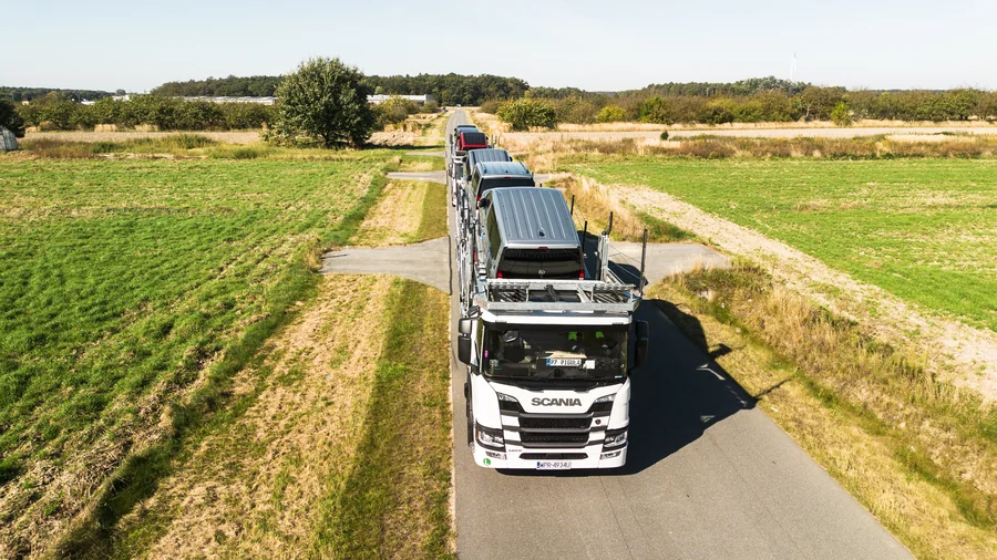 Załadowany autotransporter widziany z góry od strony kabiny na wąskiej drodze między polami.