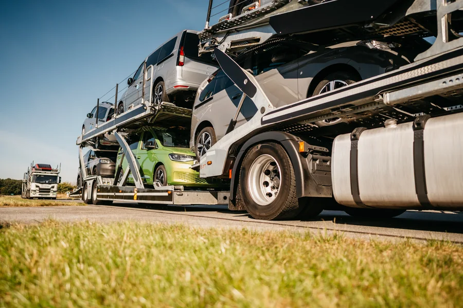 Załadowany autotransporter sfotografowany z niskiego punktu widzenia, z drugim zestawem w tle.