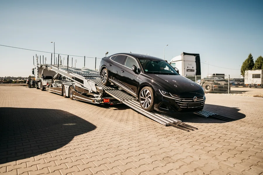 Ciemny samochód osobowy na rozłożonych rampach autotransportera na placu.